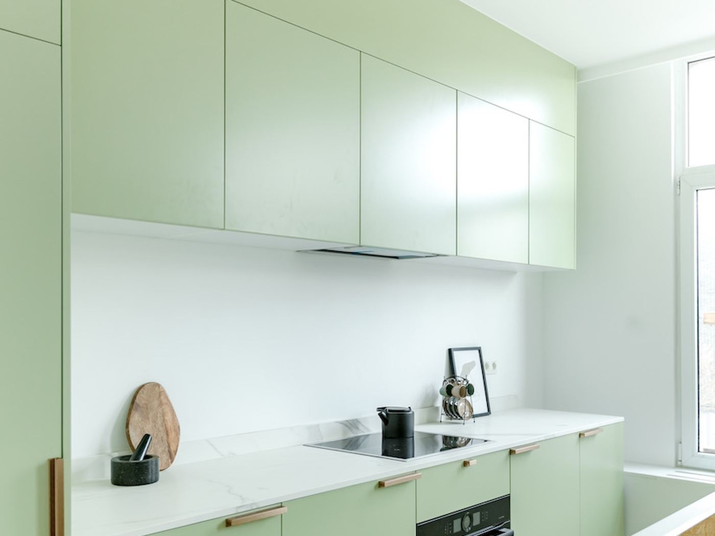 Saliegroene keuken met koperen grepen en een marmeren werkblad