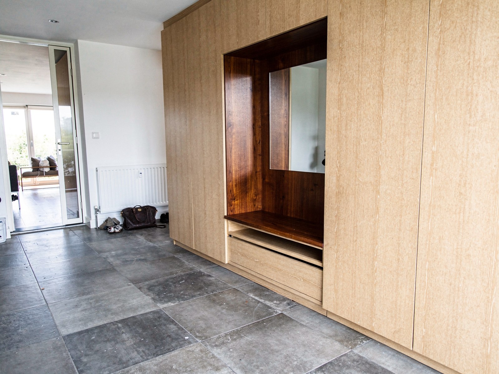 Ontwerp van een vestiaire in bleek eiken met een nis in notelaar, een spiegel en een zitbank